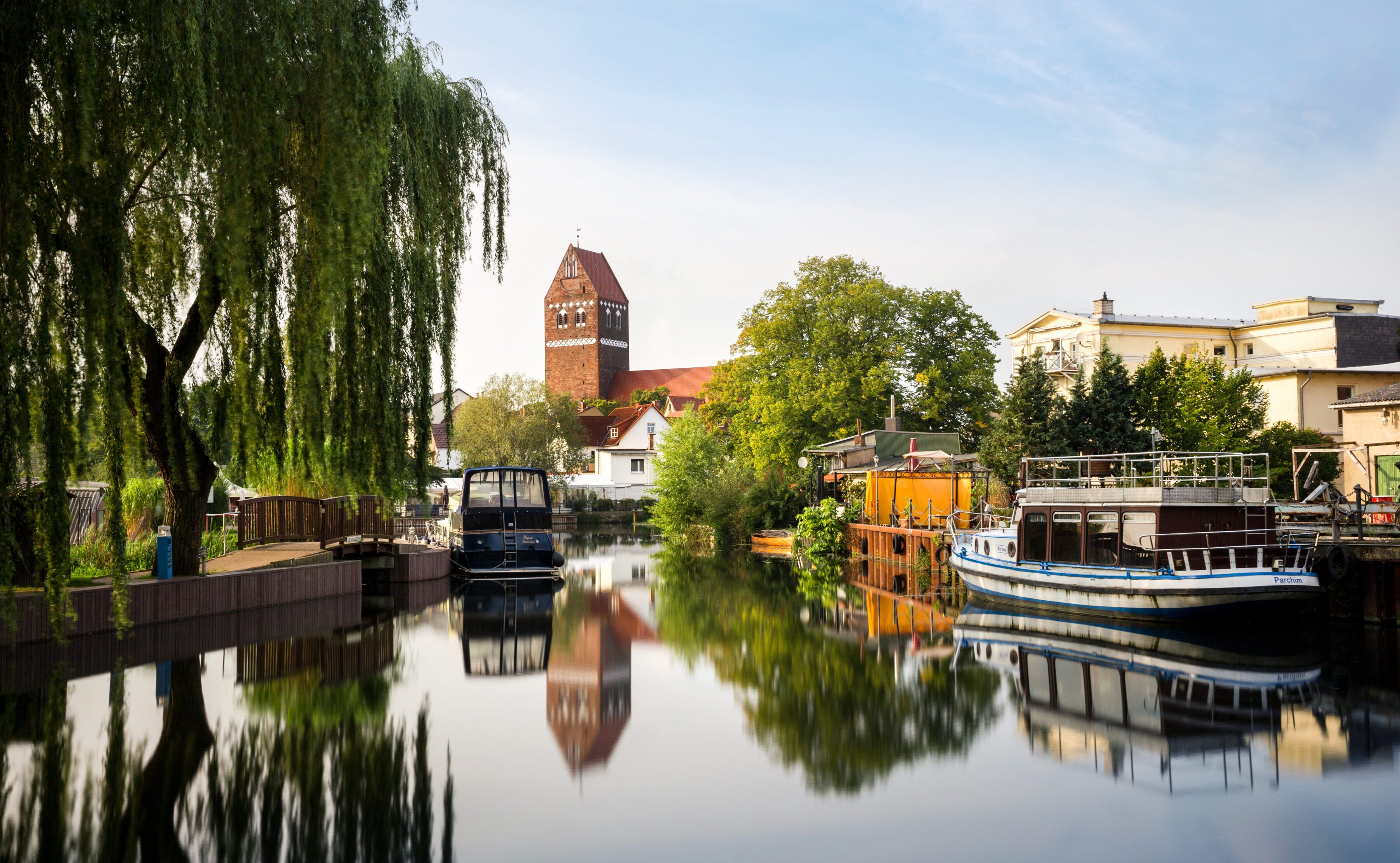 Blick auf die Kirche in Parchim, im Vordergrund ein Fluss mit Booten